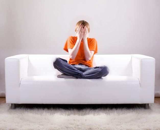 Teenager cover his face with hands on sofa