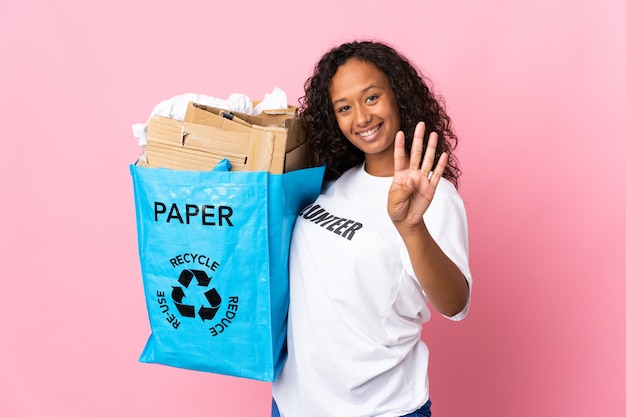 Teenager cuban girl holding a recycling bag full of paper to recycle isolated on pink  happy and counting four with fingers