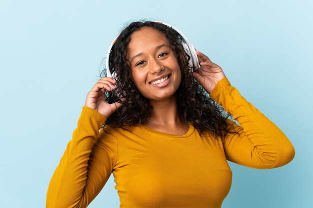 Teenager cuban girl isolated on blue wall listening music