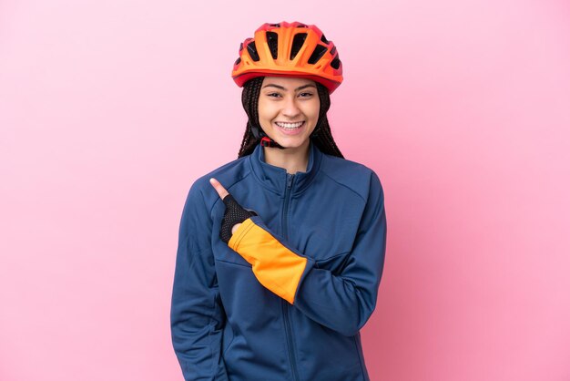 Teenager cyclist girl isolated on pink background pointing to the side to present a product