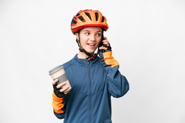 Teenager cyclist girl over isolated white background holding coffee to take away and a mobile