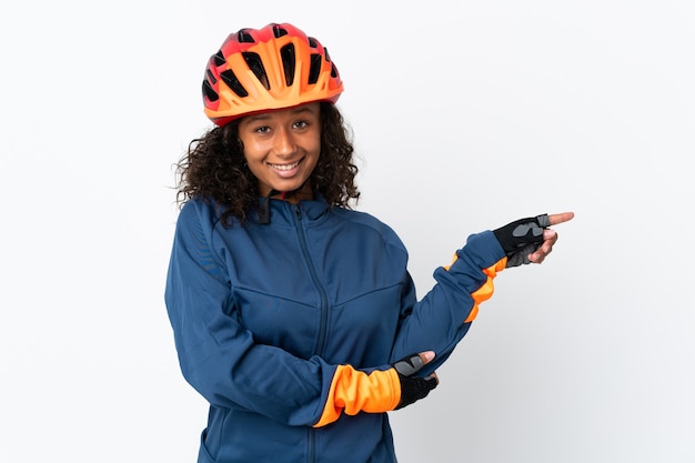 Teenager cyclist woman isolated on white background pointing finger to the side