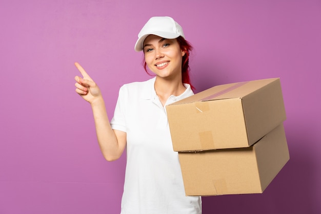 Teenager delivery girl on purple wall pointing finger to the laterals and happy