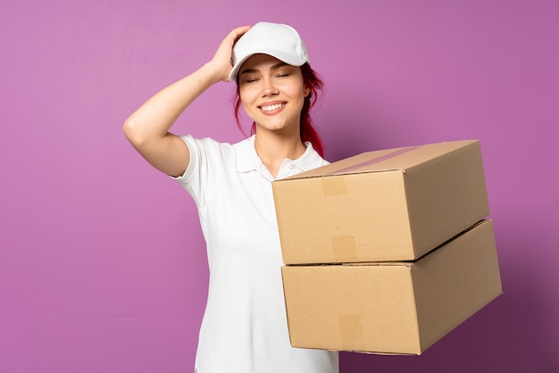 Teenager delivery woman isolated on purple wall laughing