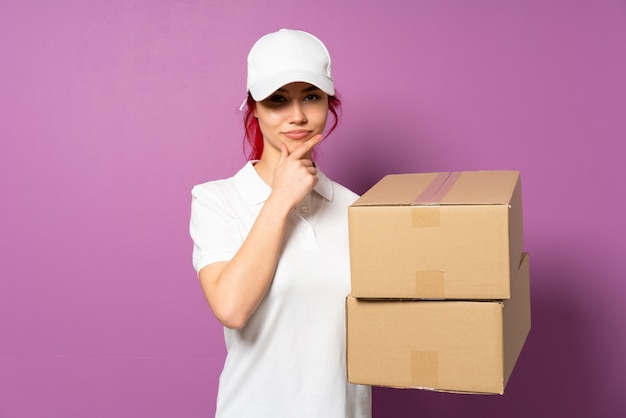 Teenager delivery woman isolated on purple wall thinking