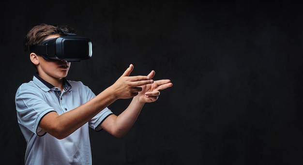 Teenager dressed in a white t-shirt playing with virtual reality glasses. Isolated on a dark background.