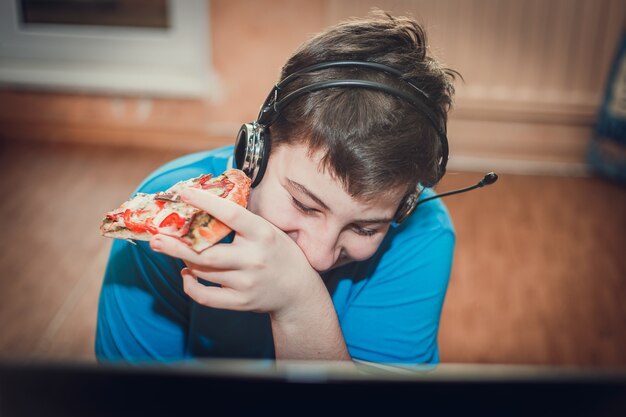 Photo teenager eating pizza sitting at a laptop.