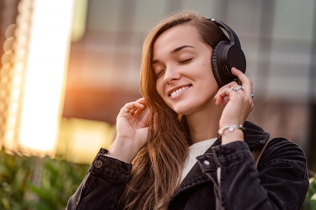 Teenager enjoys and listens to music in black wireless headphones while walking around the city