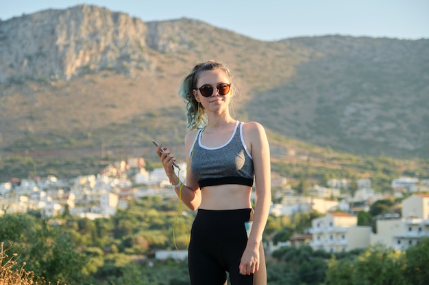 Teenager fitness runner girl with smartphone in earphones on mountain road