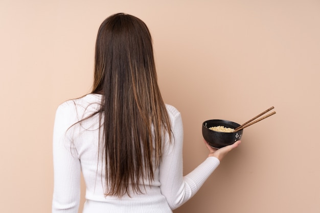 Teenager girl in back position while holding a bowl of noodles with chopsticks