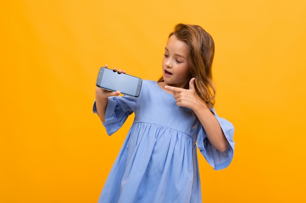 Teenager girl in a blue dress holds the phone horizontally with a layout for the site on a yellow