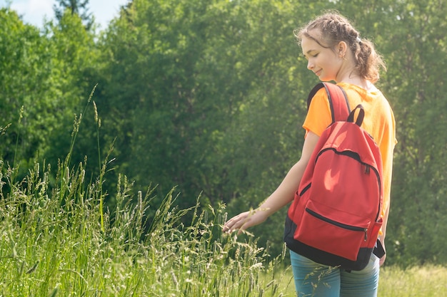 Teenager girl in a bright orange t-shirt with backpack walks in nature