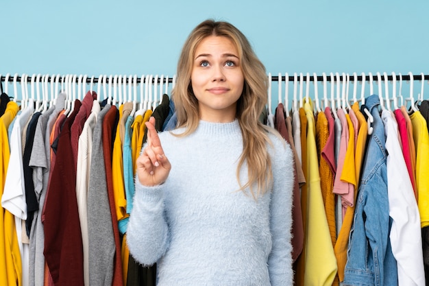 Teenager girl buying some clothes on blue with fingers crossing and wishing the best