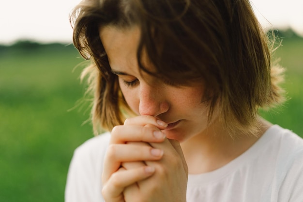 Девушка-подросток закрыла глаза, молясь. Руки сложены в молитвенной концепции за веру, духовность и религию.