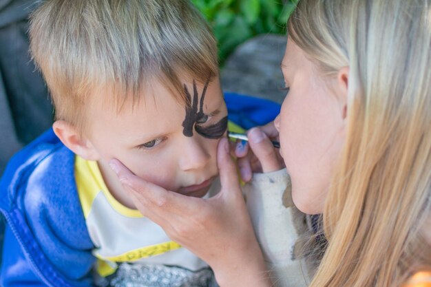 A teenager girl draws a little boy on his face