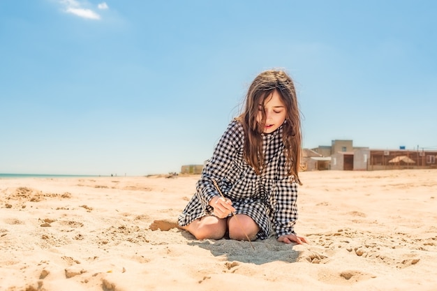 Teenager girl draws with a stick on the sand on the beach by the sea. Go to dream concept. teenage