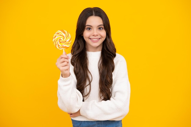 Photo teenager girl eating sugar lollypop candy and sweets for kids child eat lollipop popsicle over yellow isolated background yummy caramel candy shop happy smiling girl