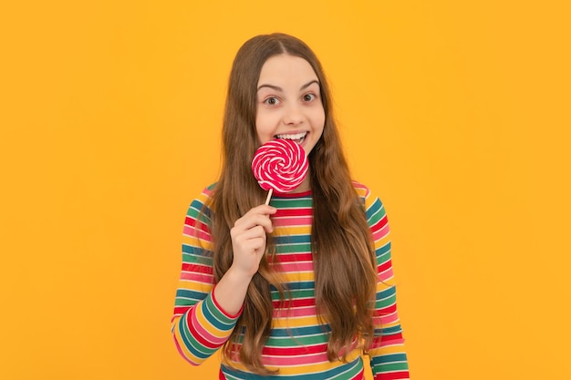 Photo teenager girl eating sugar lollypop candy and sweets for kids child eat lollipop popsicle over yellow isolated background yummy caramel candy shop