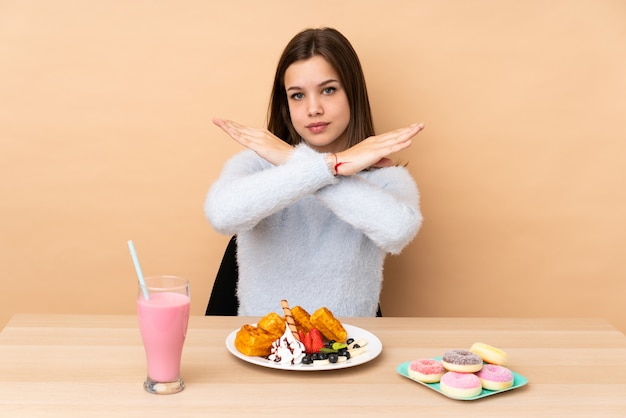 10代の少女のジェスチャーを作るベージュのワッフルを食べて