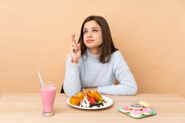 指を交差し、最高を願ってベージュの壁に分離されたワッフルを食べて10代の女の子