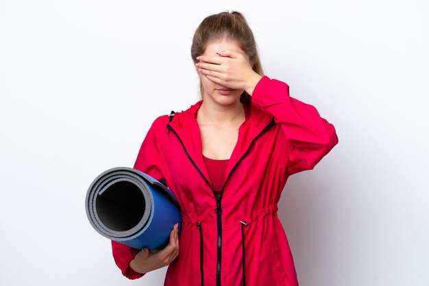 Teenager girl going to yoga classes while holding a mat isolated on white bakcground covering eyes by hands Do not want to see something