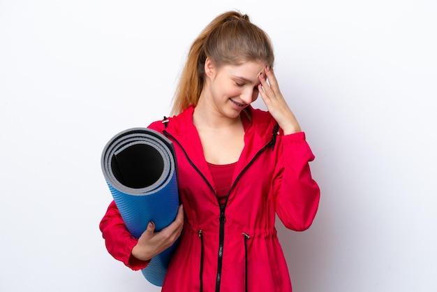 Teenager girl going to yoga classes while holding a mat isolated on white bakcground laughing