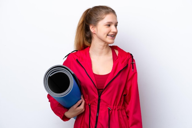 Teenager girl going to yoga classes while holding a mat isolated on white bakcground looking side