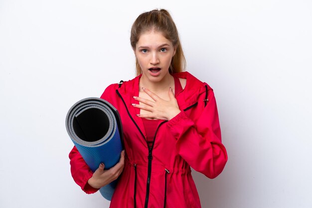 Teenager girl going to yoga classes while holding a mat isolated on white bakcground surprised and shocked while looking right