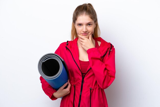 Teenager girl going to yoga classes while holding a mat isolated on white bakcground thinking