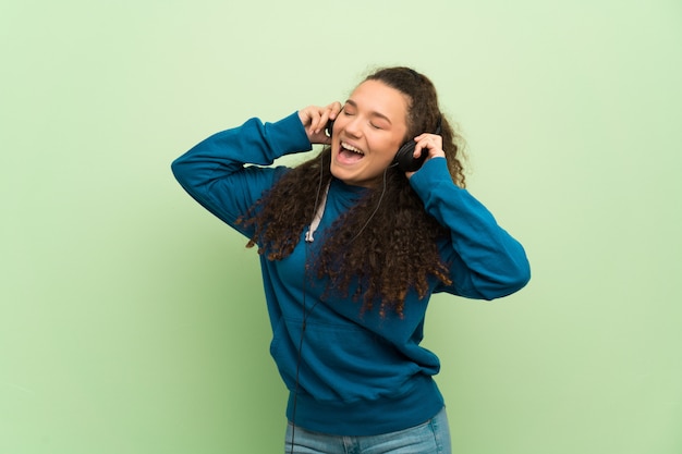 Teenager girl over green wall listening to music with headphones