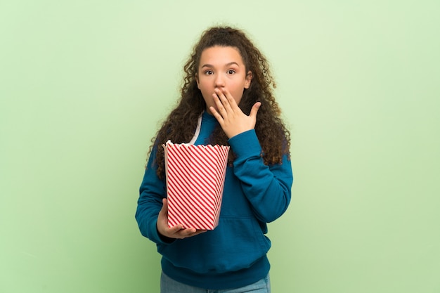 緑の壁の上のティーンエイジャーの女の子が驚いて、ポップコーンを食べる