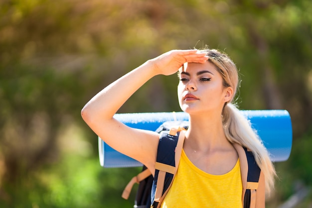 Teenager girl hiking at outdoors looking far away with hand to look something