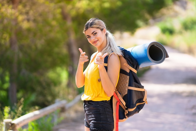 Teenager girl hiking at outdoors pointing to the front and smiling