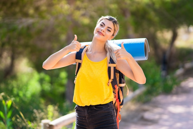 ジェスチャーと笑みを浮かべて親指で屋外でハイキングのティーンエイジャーの女の子