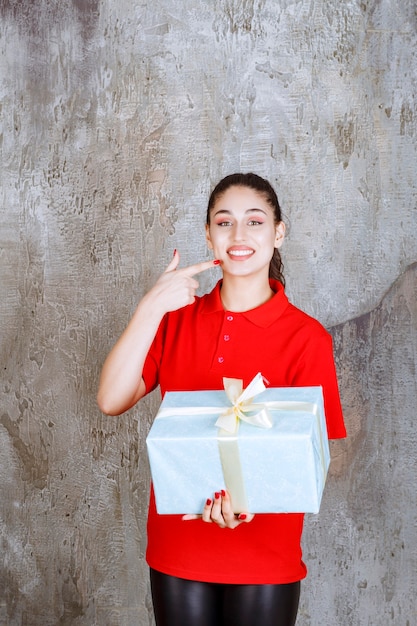 Teenager girl holding a blue gift box wrapped with white ribbon