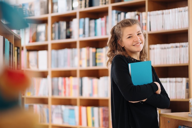 Teenager girl holding a book among many books