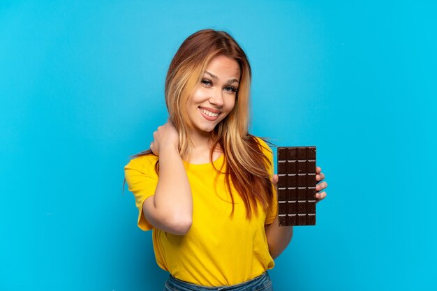 Teenager girl holding chocolat over isolated blue background laughing