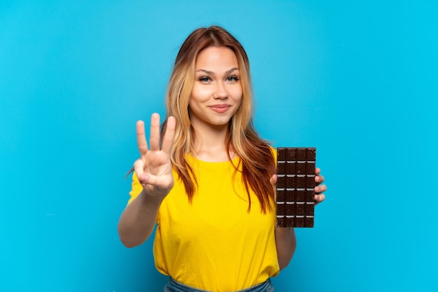 Teenager girl holding chocolat isolated happy and counting three with fingers