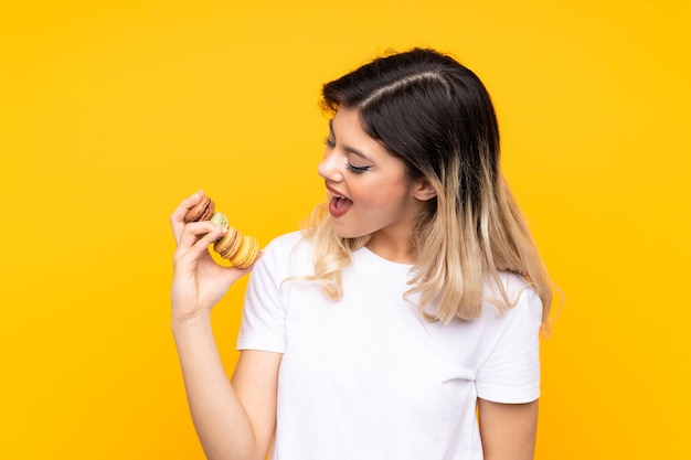 Teenager girl holding colorful French macarons and celebrating a victory