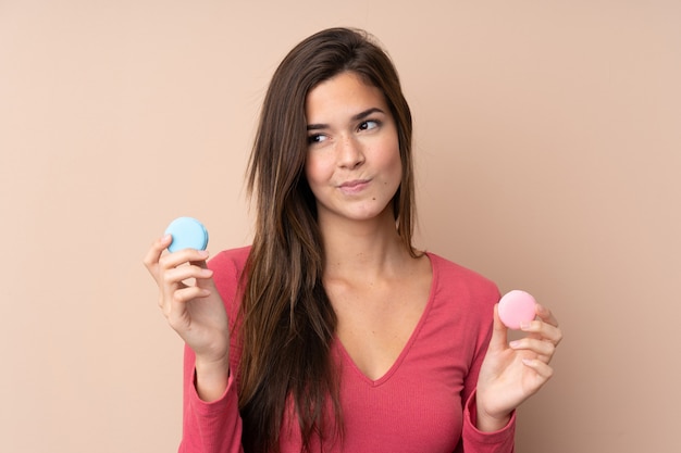 Teenager girl holding colorful French macarons and thinking