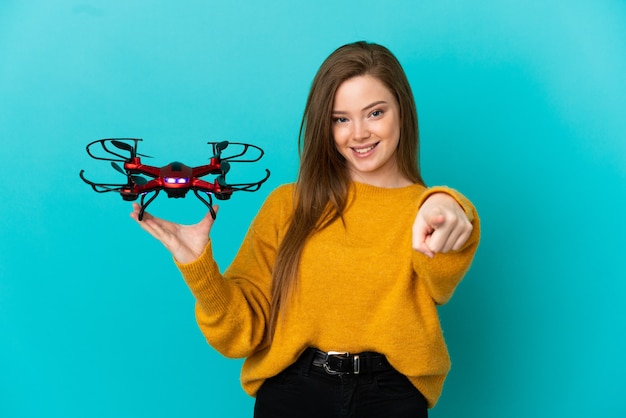 Teenager girl holding a drone over isolated blue background surprised and pointing front