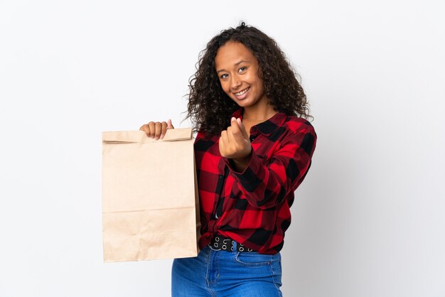 Teenager girl holding a grocery shopping bag to takeaway isolated on white background making money gesture