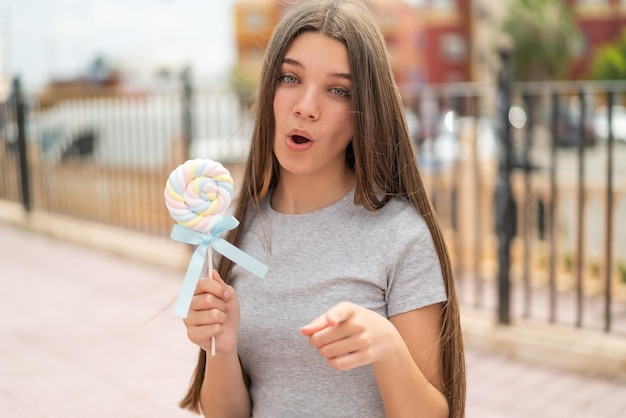 Foto ragazza dell'adolescente che tiene un lecca-lecca sorpreso e che indica la parte anteriore