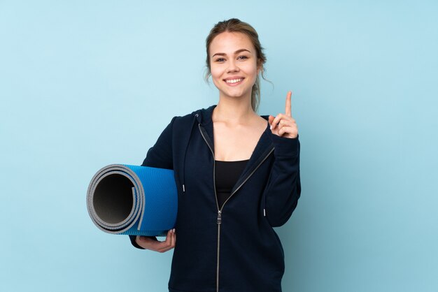 Teenager girl holding mat isolated on blue pointing up a great idea