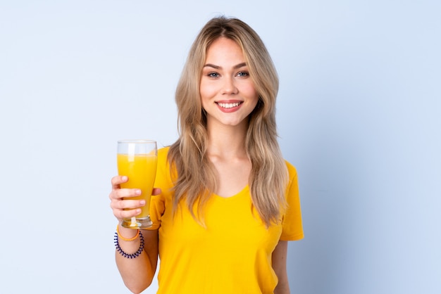 Teenager girl holding an orange juice on blue wall smiling a lot