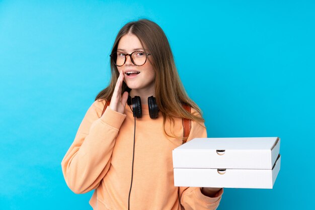  teenager girl holding pizzas over isolated blue wall shouting with mouth wide open