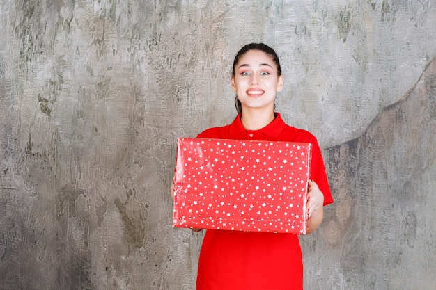 Девушка-подросток держит красную подарочную коробку с белыми точками на ней.
