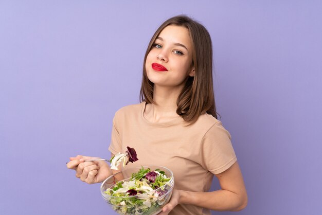 Teenager girl holding salad isolated on purple wall