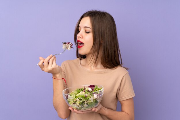 Девушка подростка держа салат изолированный на фиолетовой стене