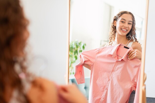 사진 실내 거울 앞에 서 있는 셔츠를 들고 있는 10대 소녀